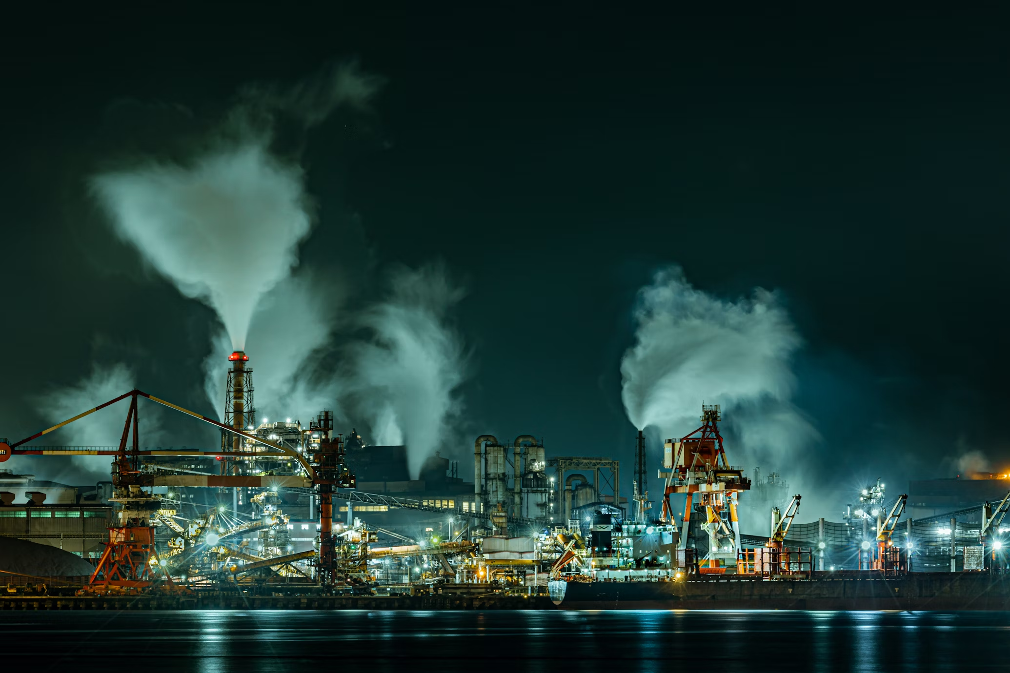 A factory with smoke billowing from its chimneys, illuminated by bright explosion-proof lighting fixtures