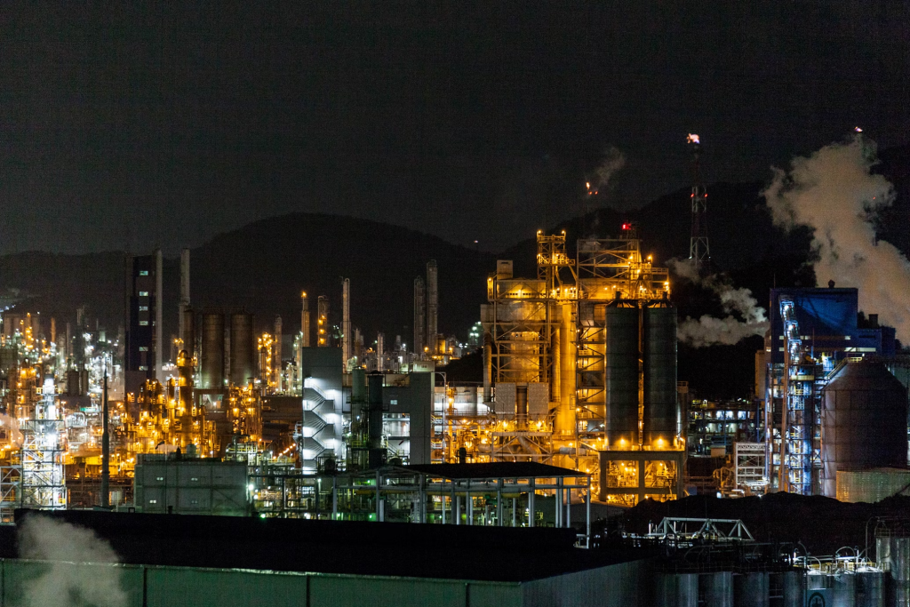 Night view of a large refinery, featuring bright explosion-proof lights and smoke rising from the chimneys.