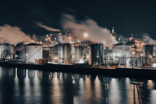 An industrial facility at night, featuring bright LED explosion-proof lights and smoke emitting from the stacks.