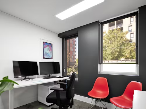 A clean office featuring a desk, chair, computer, and panel light illuminating the workspace.