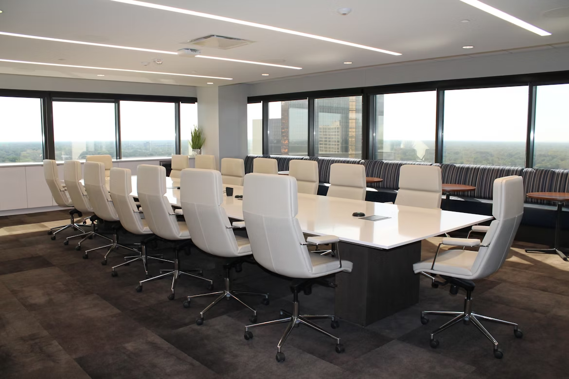 A conference room featuring white chairs, a large window, and bright office lights illuminating the space.