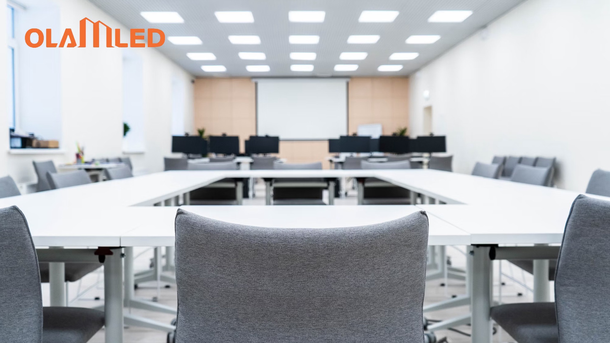 A conference room setup with chairs, a projector screen, and an overhead led panel light illuminating the space.