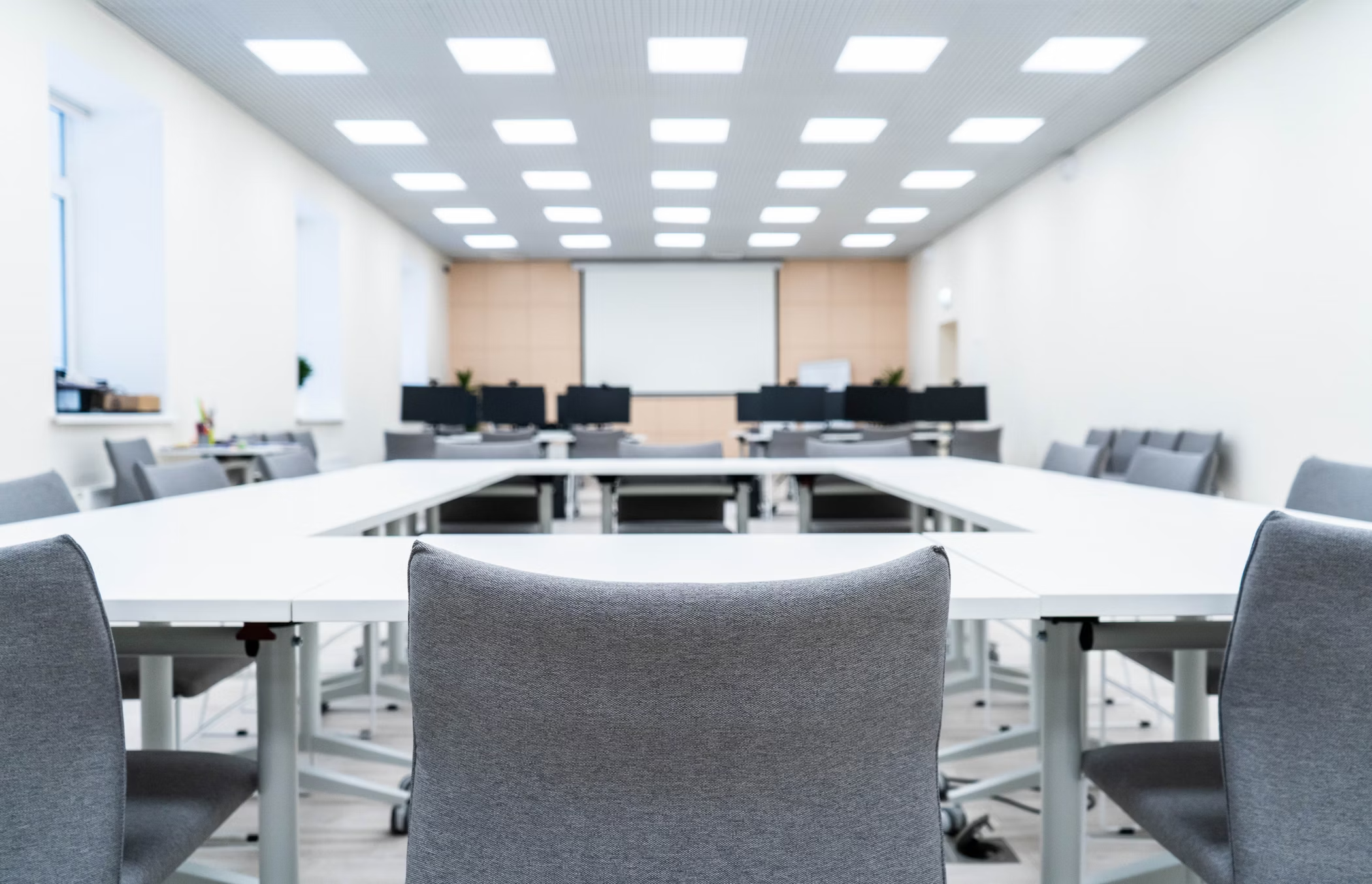 A conference room setup with chairs, a projector screen, and an overhead led panel light illuminating the space.