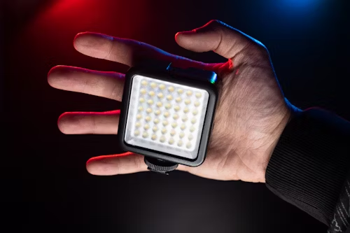 A hand displays a small led light, contrasting with dynamic red and blue lighting behind it.