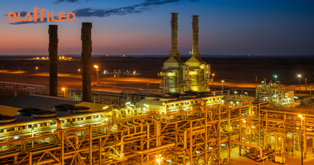 A large oil refinery at sunset, glowing with bright explosion proof lights as the day transitions to night.