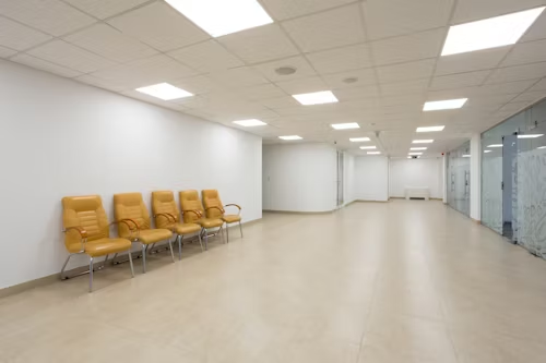 A long hallway featuring yellow chairs, white walls, and panel lighting illuminating the space