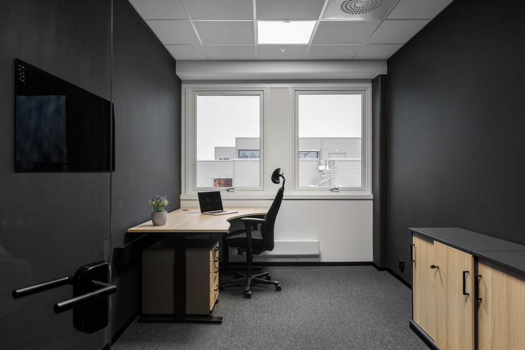 A modern office with black walls, a desk, and an led panel light providing bright illumination.
