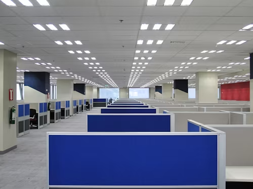 A modern office with blue and white cubicles, brightly lit by overhead panel lights