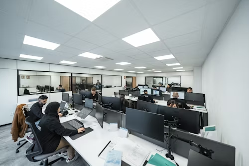A spacious office filled with people working diligently at their desks, surrounded by modern decor and bright lighting