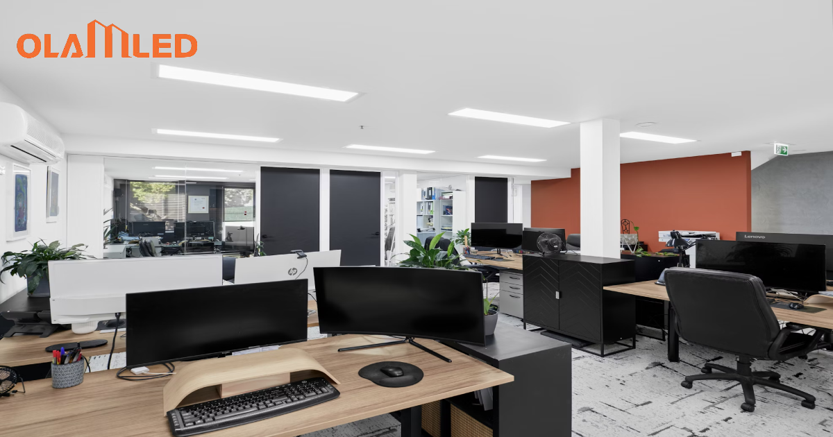 A spacious open office featuring multiple desks, computers, and bright panel lighting.