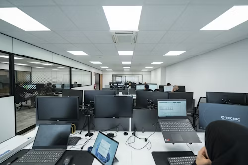 A spacious open office filled with computers and people, illuminated by bright led panel lights.