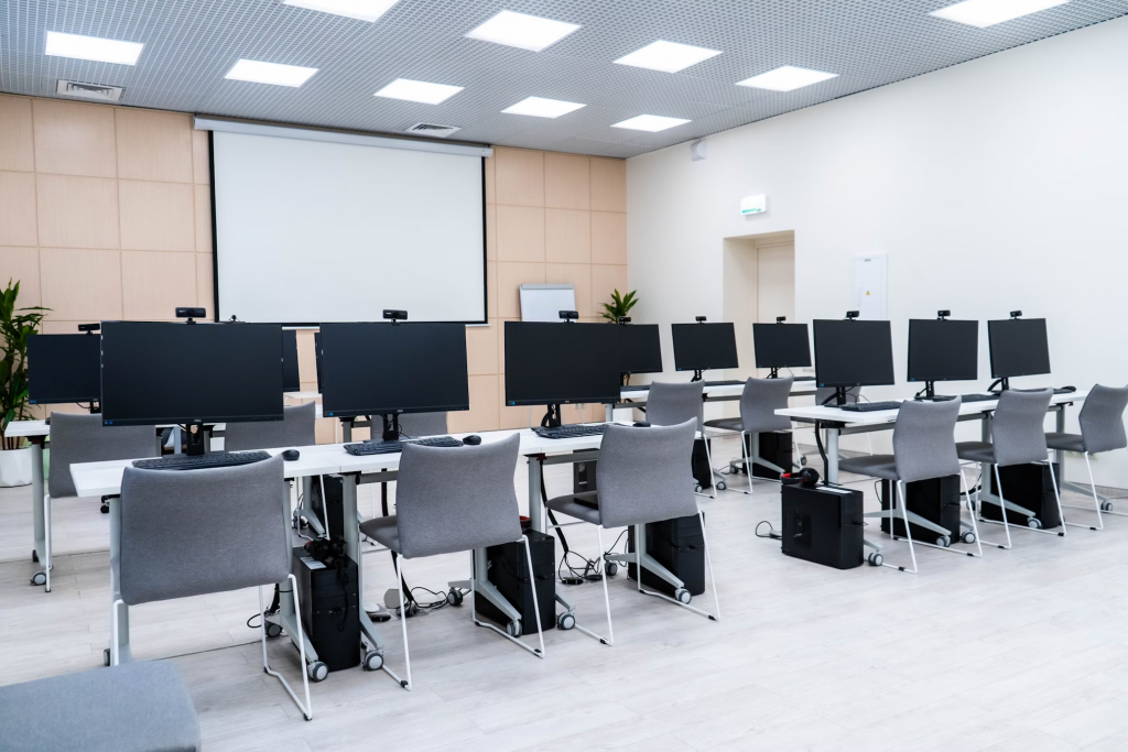 A well lit classroom with multiple computers and chairs, enhanced by an led panel light overhead.