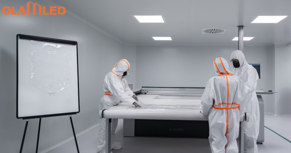 In a cleanroom, three people in protective suits work together at a large table.