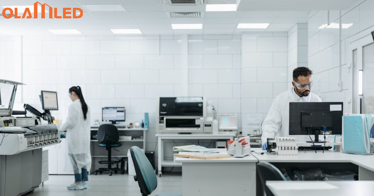 Two individuals working on computers in a cleanroom lab, illuminated by bright cleanroom lighting.